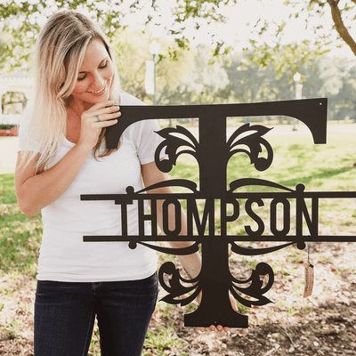 Woman holding a decorative metal sign with 'THOMPSON' on it outdoors.